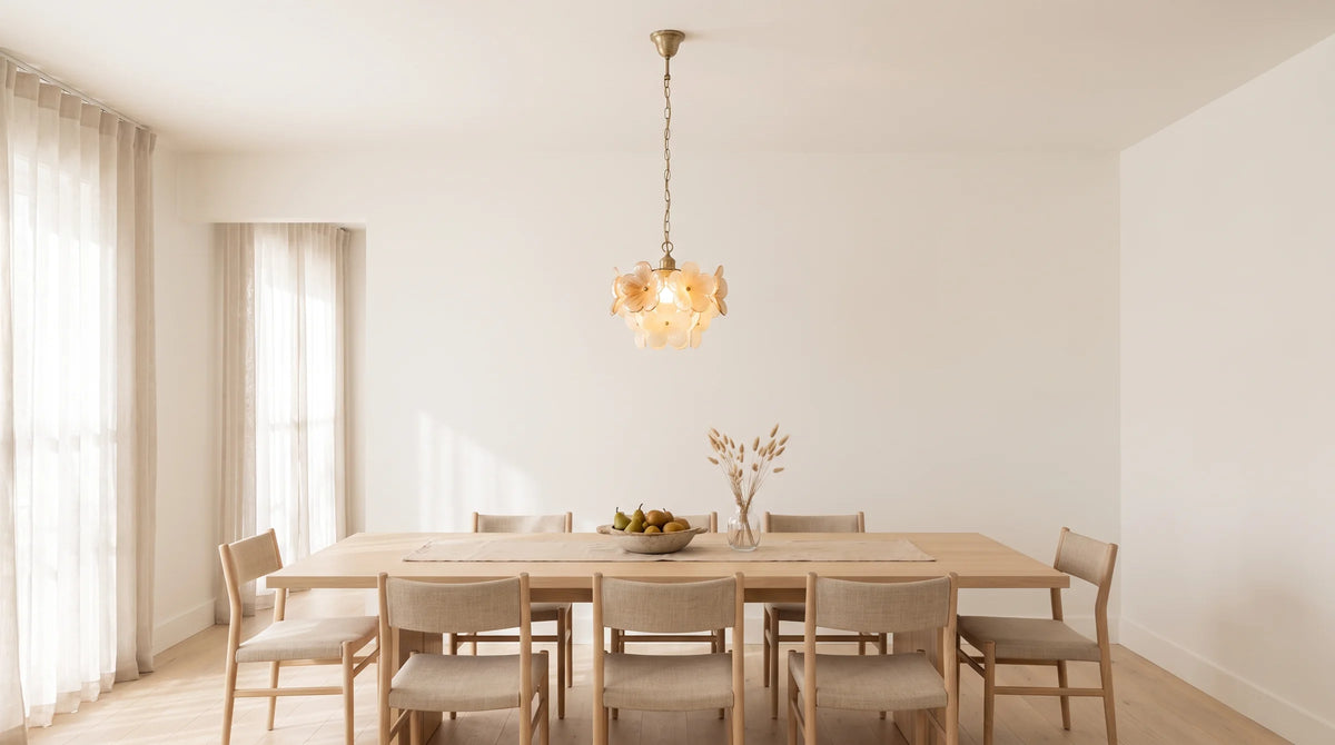 A pale oak dining table below a glass flower pendant in morning light